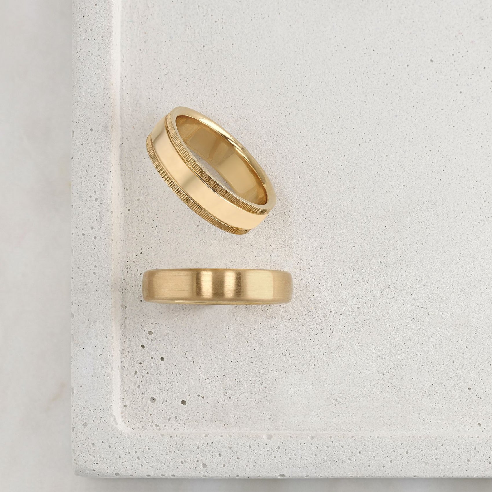 Two gold rings on a textured white surface